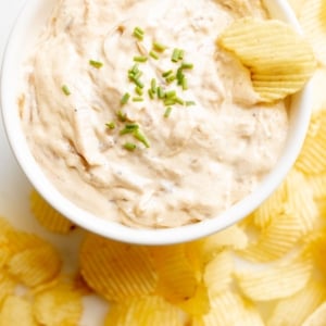 A bowl full of homemade french onion dip, surrounded by potato chips.