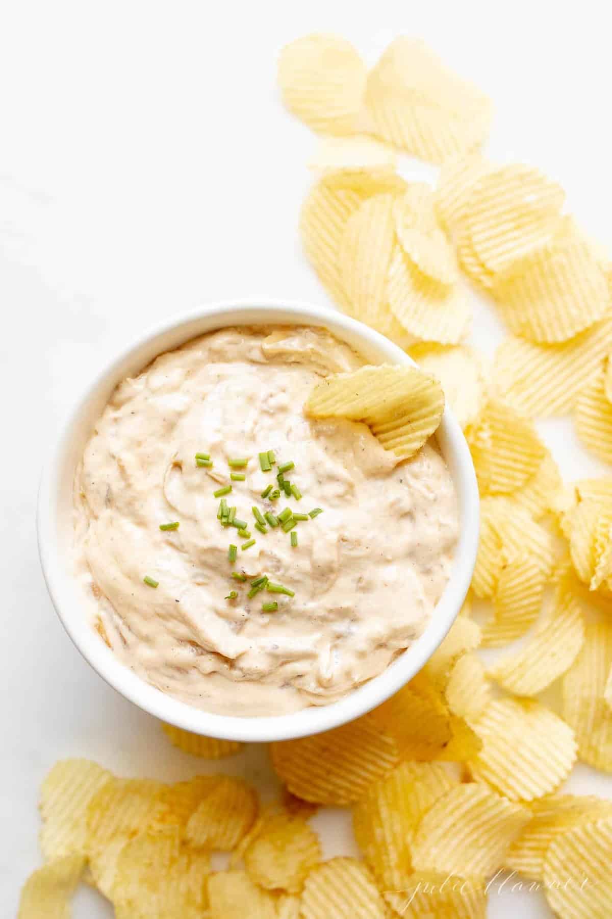 chip dipped into bowl of french onion dip surrounded by crinkle chips