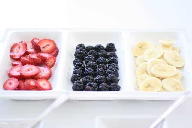 A white partitioned tray full of fruit for mini fruit pizza cookies.