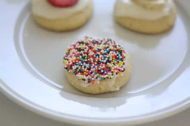 A white plate with sugar cookies, some have fruit toppings and some have sprinkles