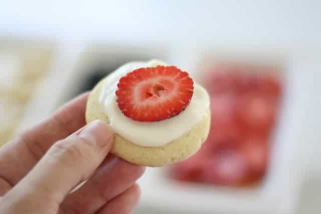 A hand holding a sugar cookie with a slice of strawberry on top.