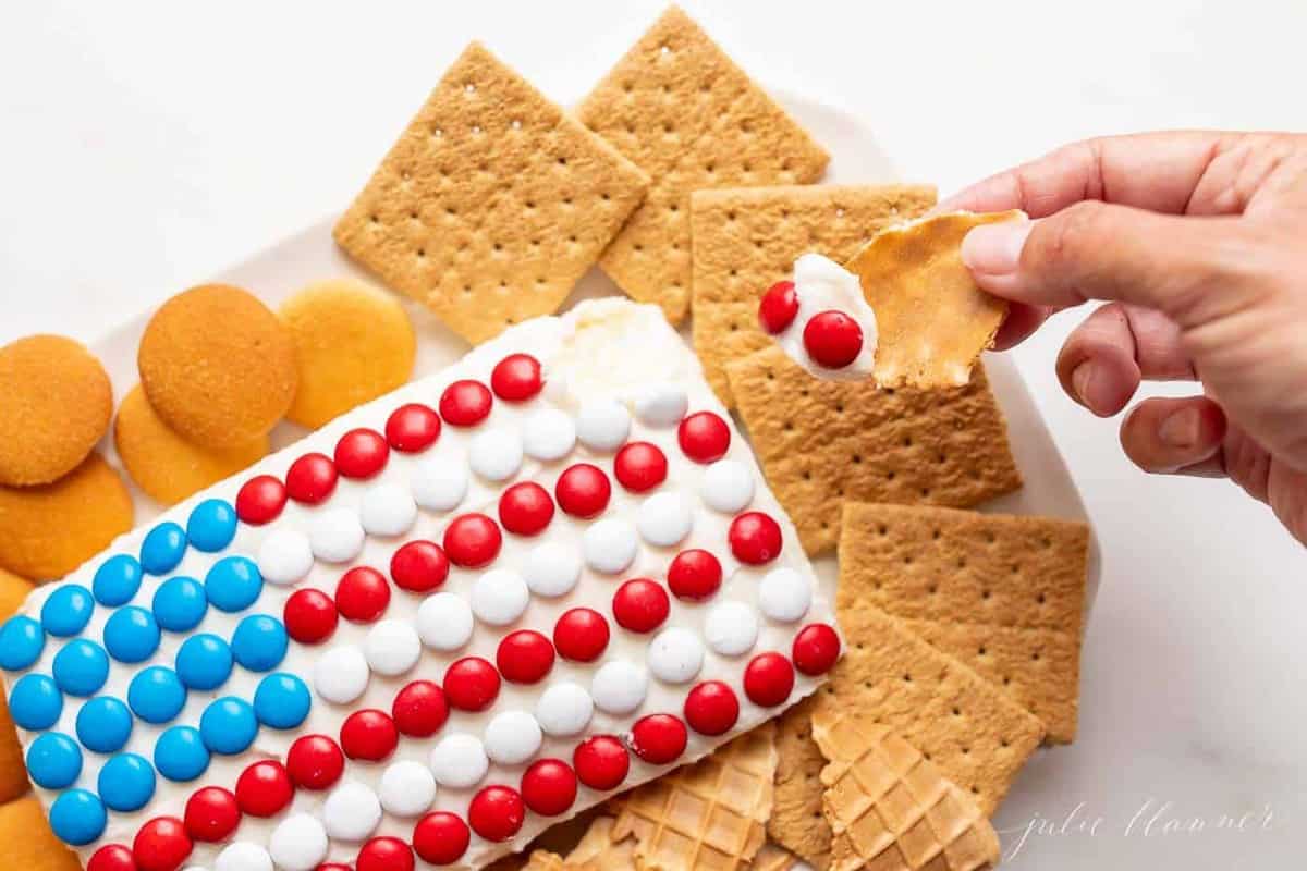 A frosted fourth of july flag dessert, covered in m&ms, crackers surrounding.