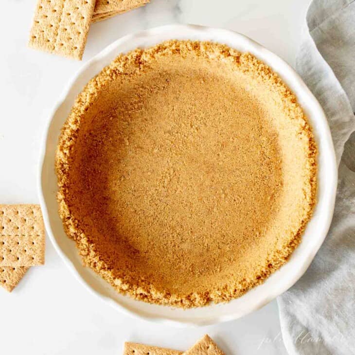 graham cracker pie crust in white pie dish with graham crackers surrounding it