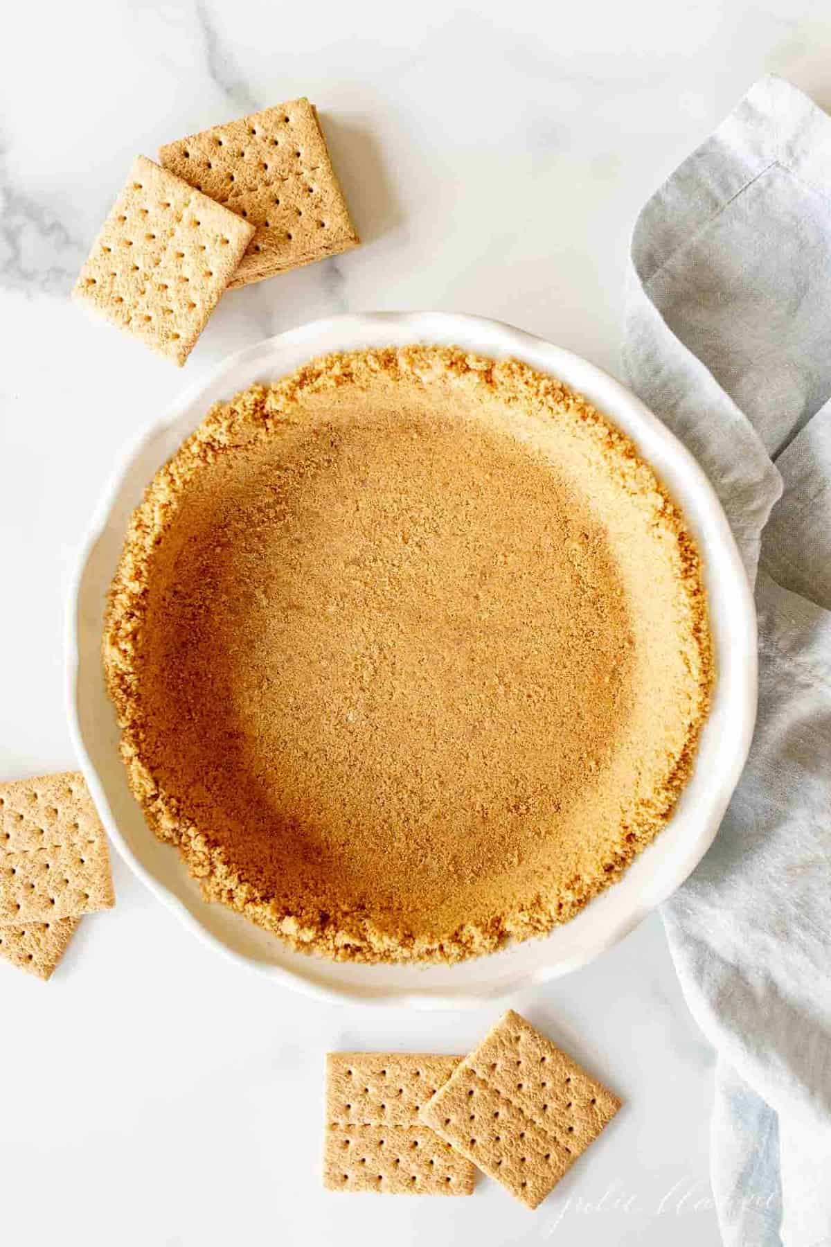 graham cracker crust in white pie dish with crackers surrounding it