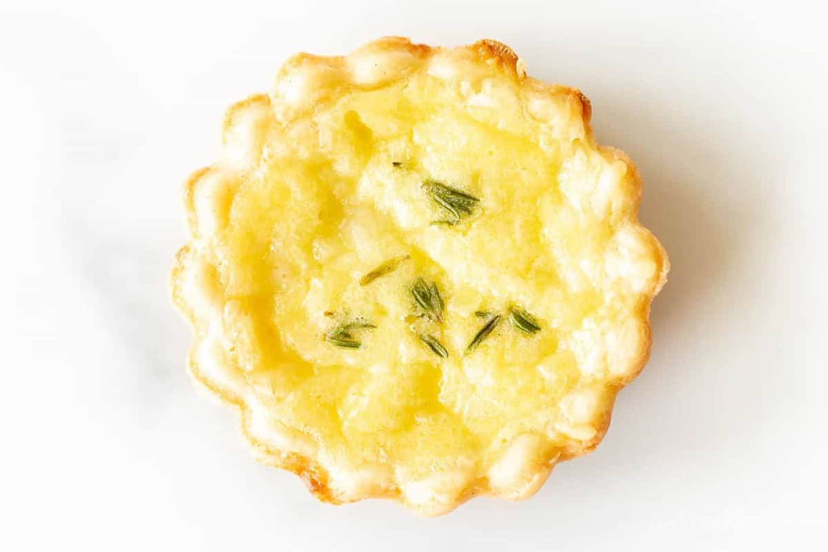 A small cheddar cheese tart topped with fresh herbs on a marble surface.