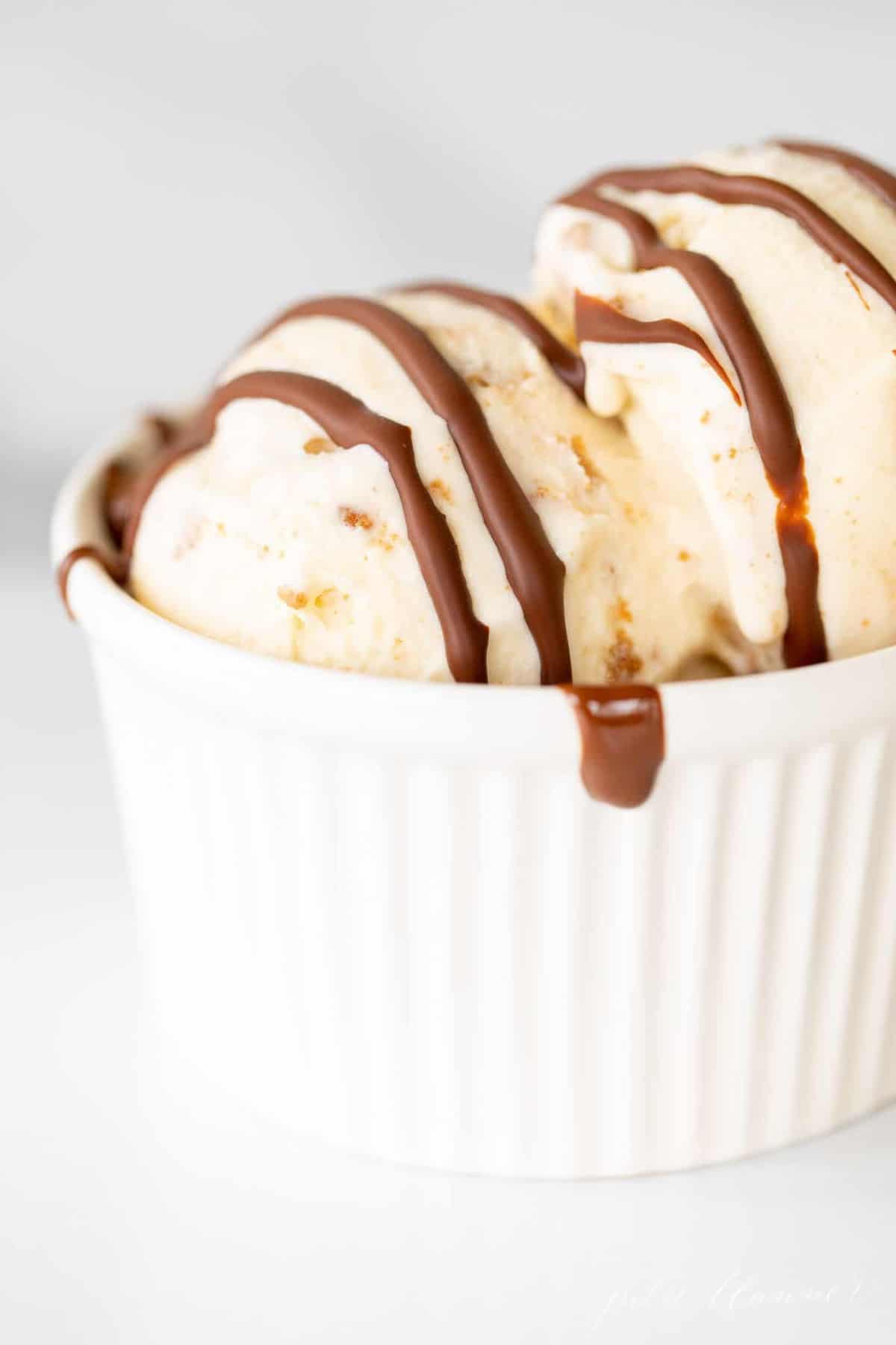 A white ramekin filled with vanilla ice cream and covered with dripping chocolate homemade magic shell.