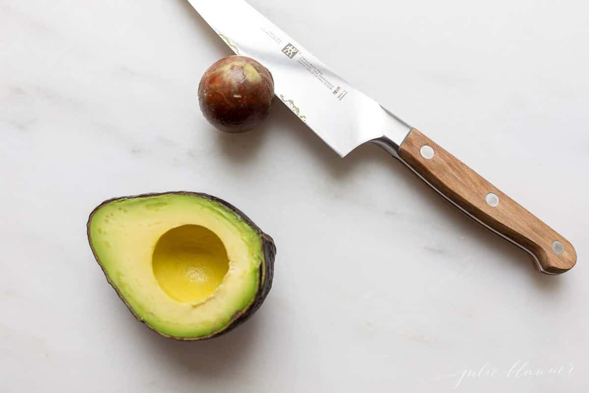 An avocado cut in half, while the knife has the pit on it.