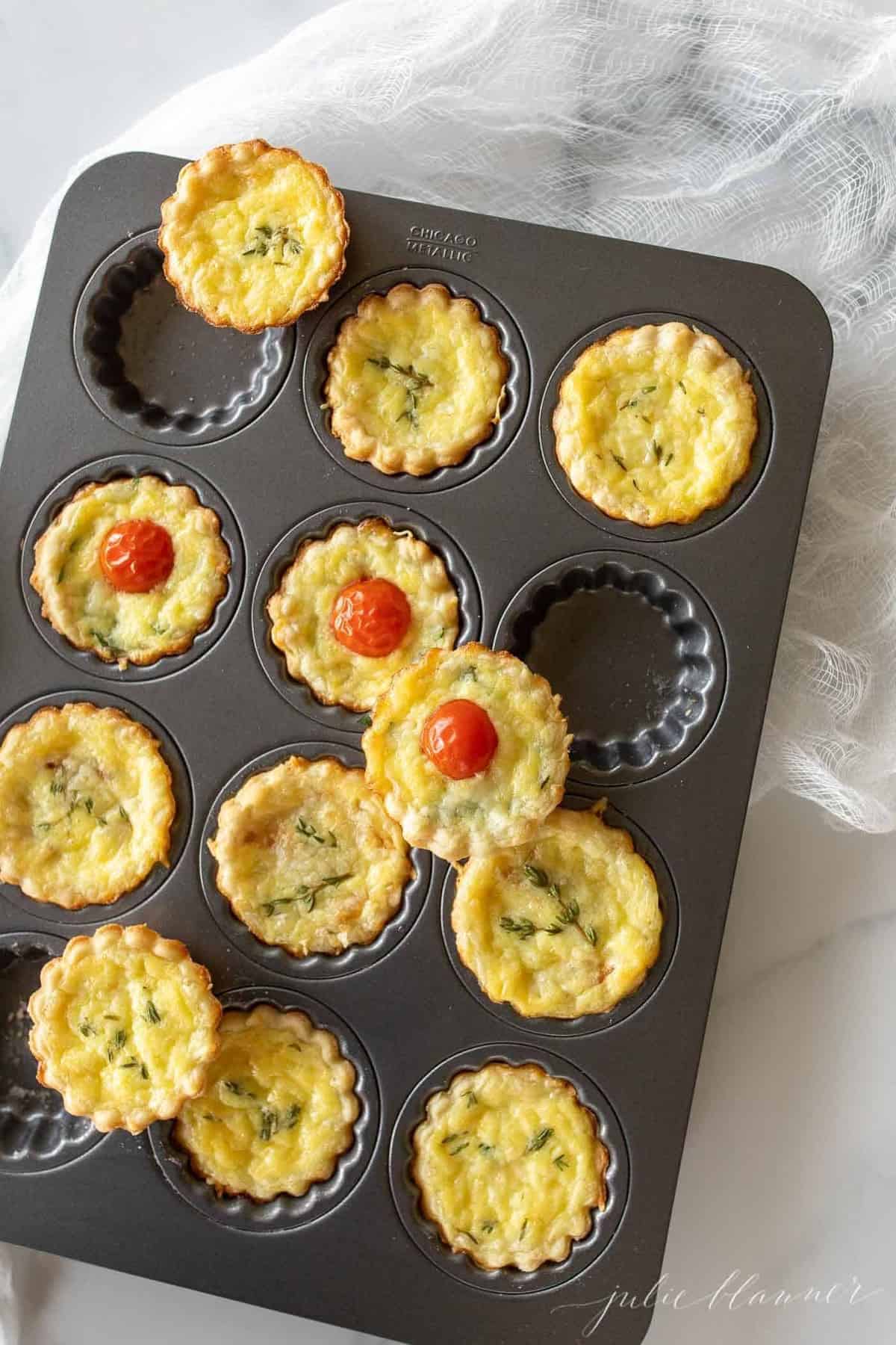 A muffin pan with cheddar cheese tarts in each cup.