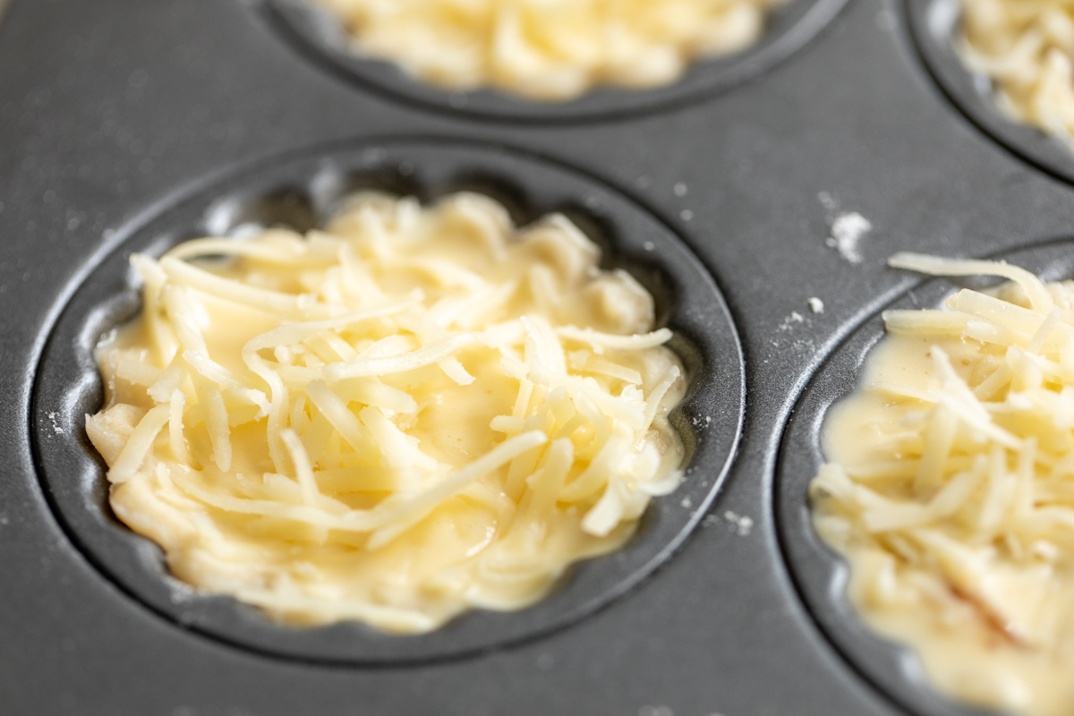 A mini cheese tart crust inside a muffin tin, prior to baking.