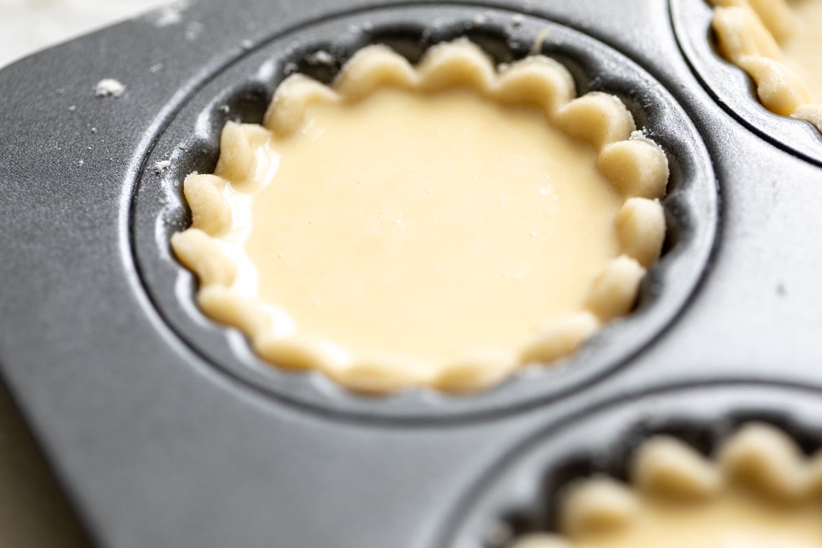 A mini cheese tart inside a muffin tin, prior to baking.