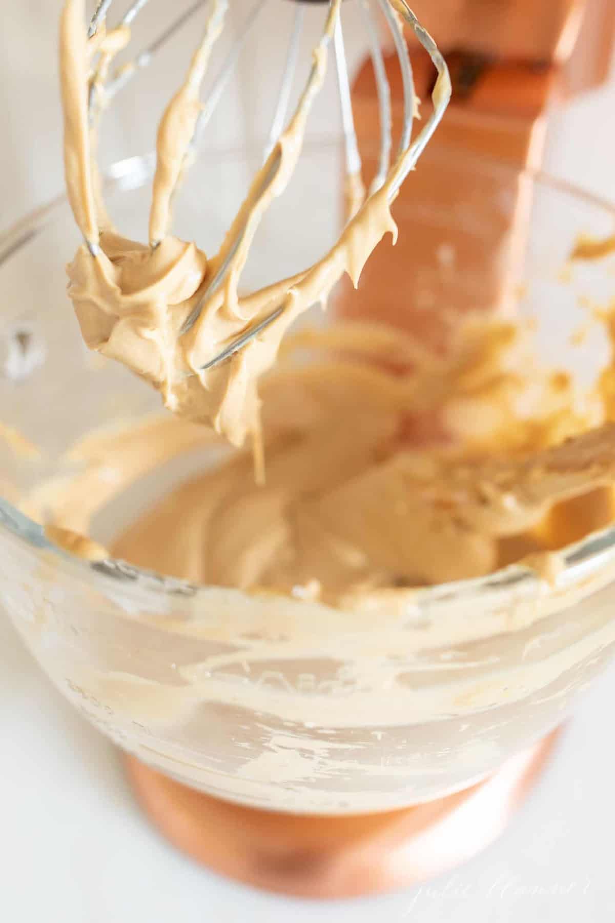 A stand mixer with a fitted glass bowl, filled with cookie butter cheesecake filling.
