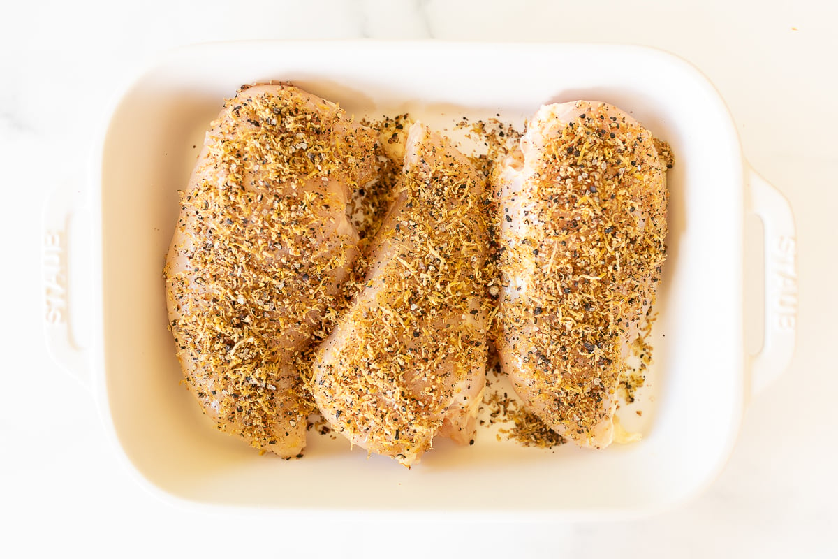 Lemon pepper chicken in a white baking dish before cooking.