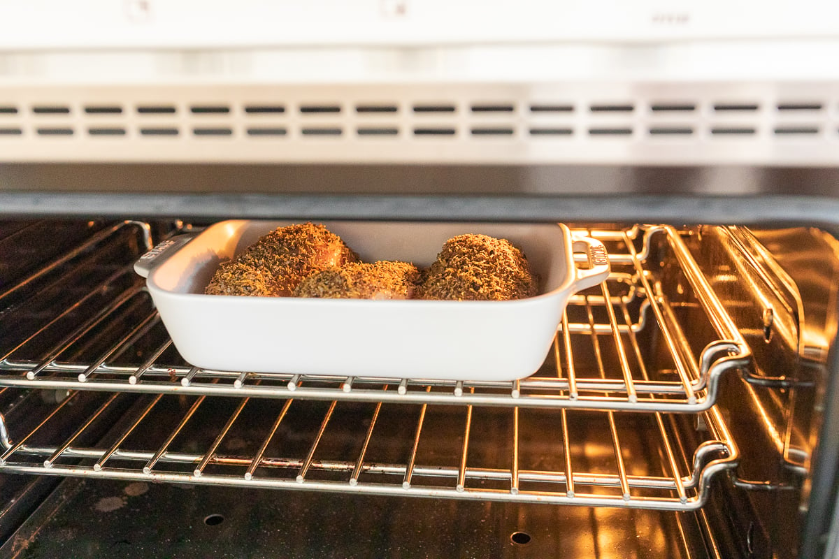 Lemon pepper chicken in a white baking dish in the oven.
