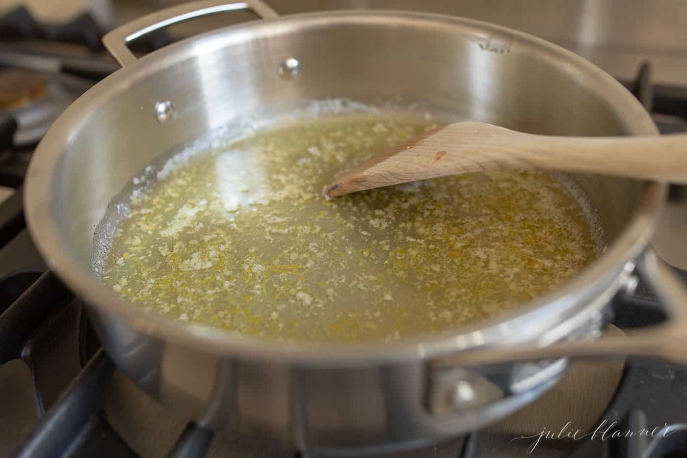 A silver pan on a stove top, melted butter and garlic being stirred with a wooden spatula.