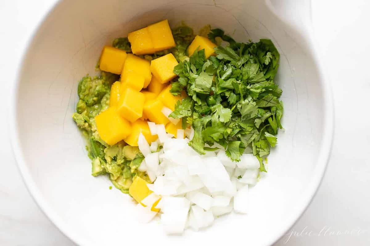 Looking into a white bowl with fresh ingredients for mango guacamole.