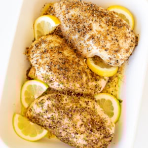Baked lemon pepper chicken in a white baking dish.