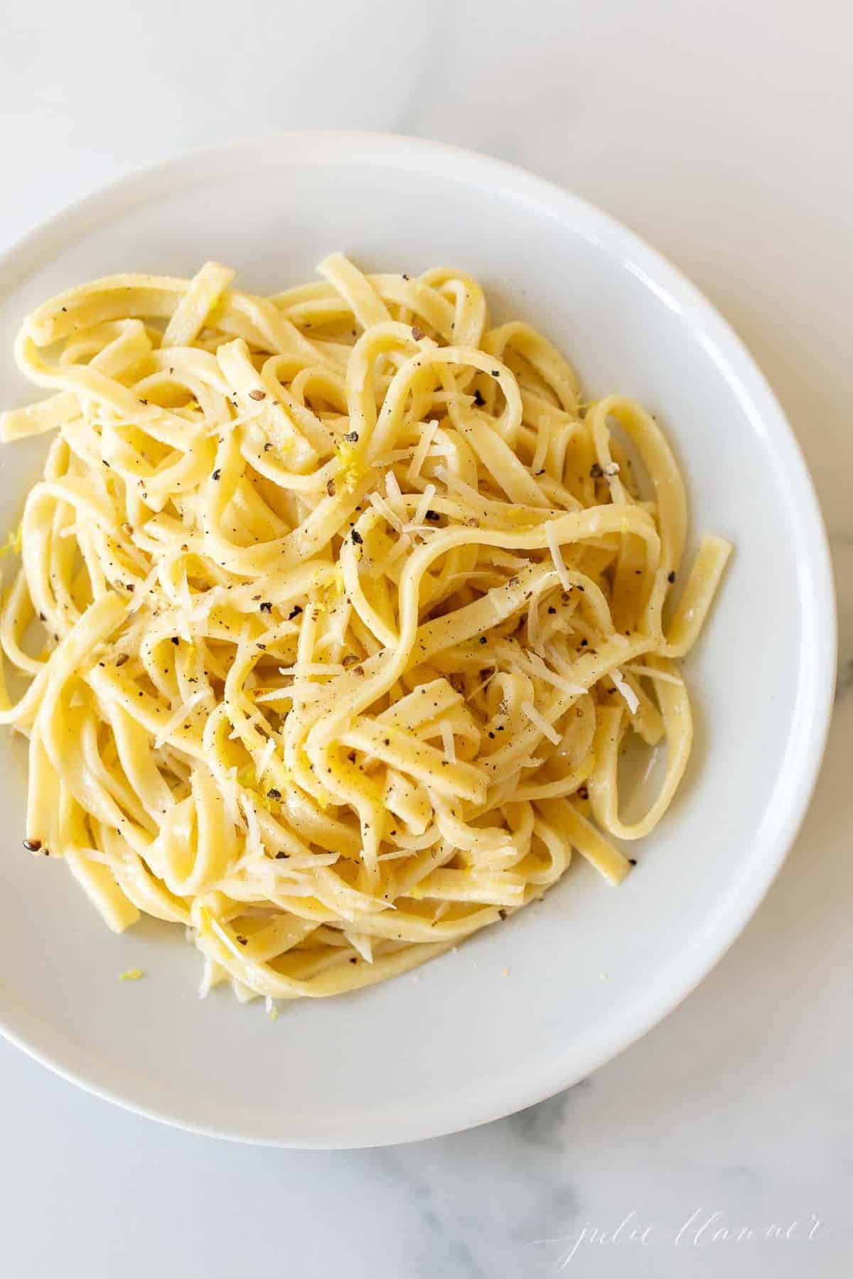 A white plate with a bowl full of lemon pepper pasta.