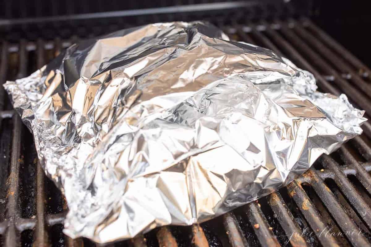 A chunk of aluminum foil on a grill, baked salmon with lemon inside.