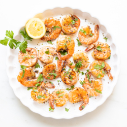 Lemon pepper shrimp on a round white serving platter.