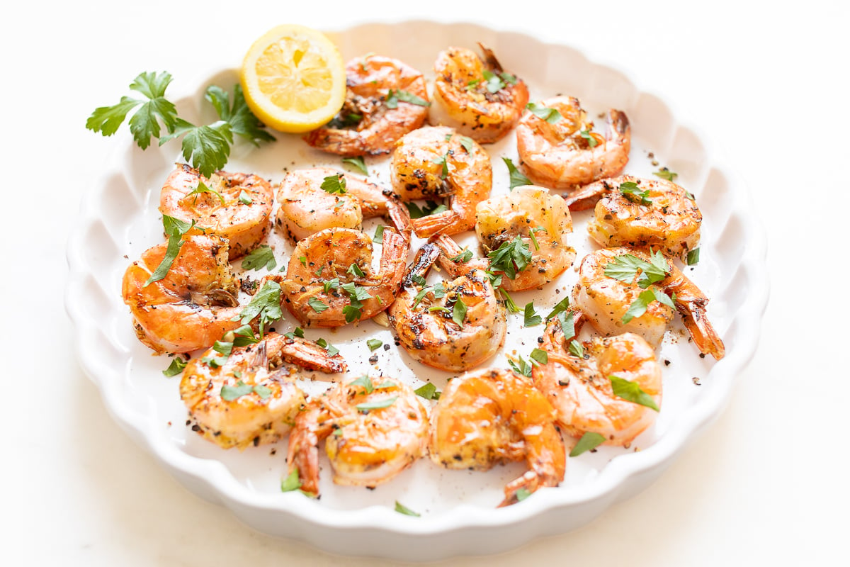 A round plate full of cooked lemon pepper shrimp.