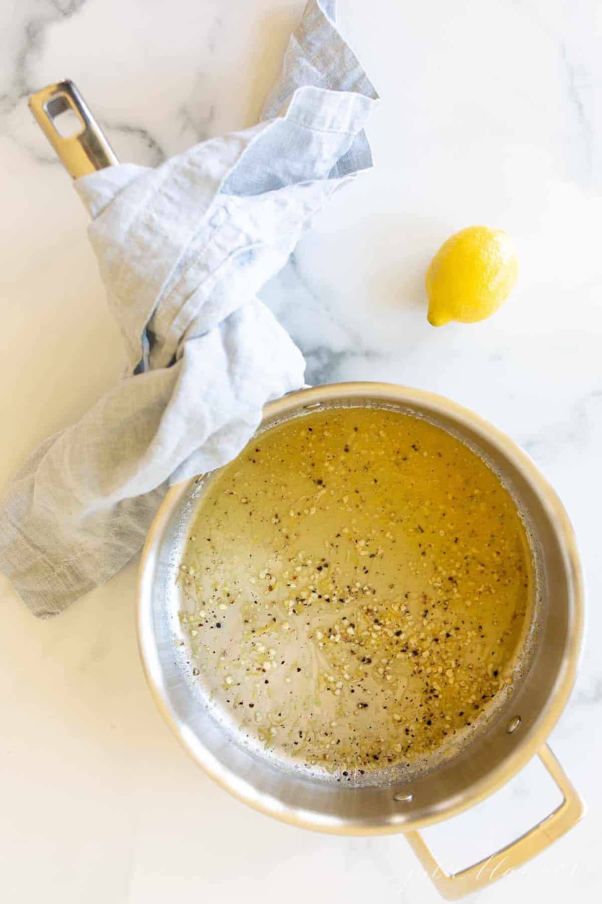A saucepan on a marble surface, lemon pepper sauce inside.
