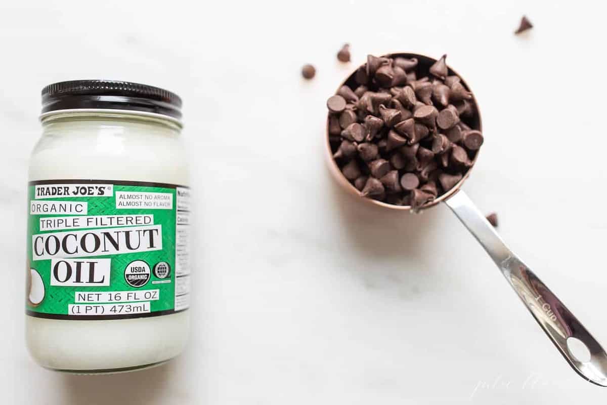 A bottle of coconut oil and a cup of chocolate chips.