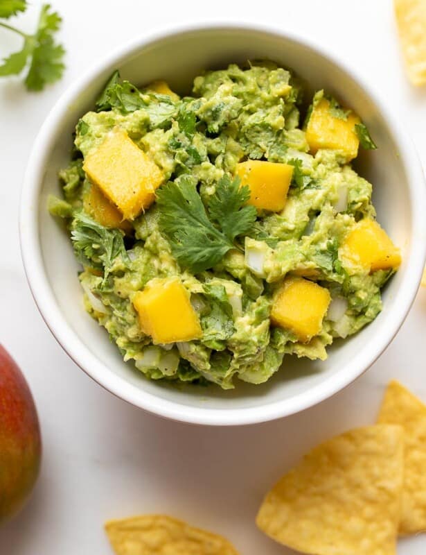 A bowl of mango guacamole and its ingredients around it