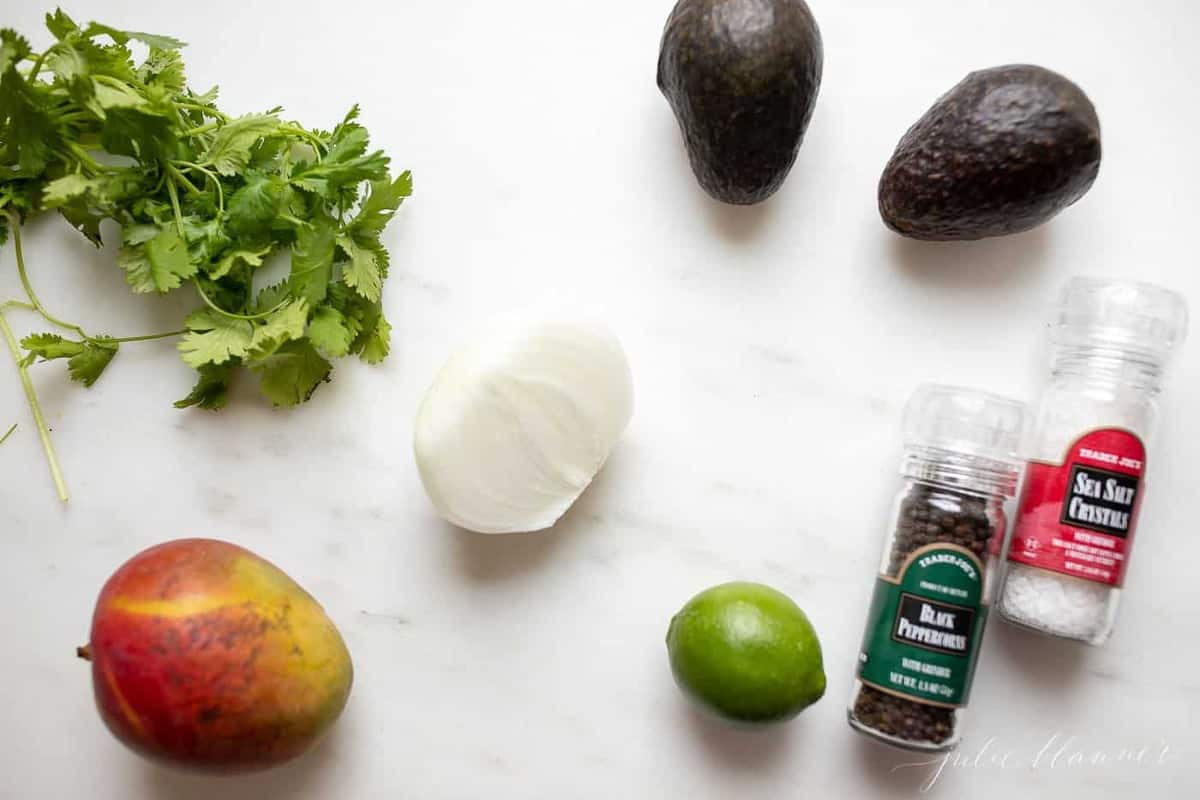 A marble surface with fresh ingredients for mango guacamole.