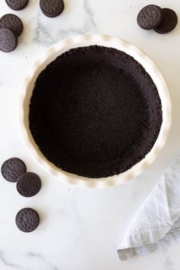 A white ceramic pie dish with an oreo crust recipe inside, oreos to the side.