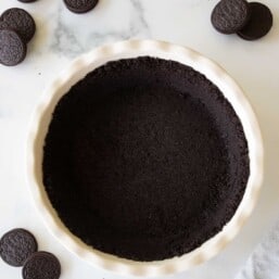 A white ceramic pie dish with an oreo crust recipe inside, oreos to the side.