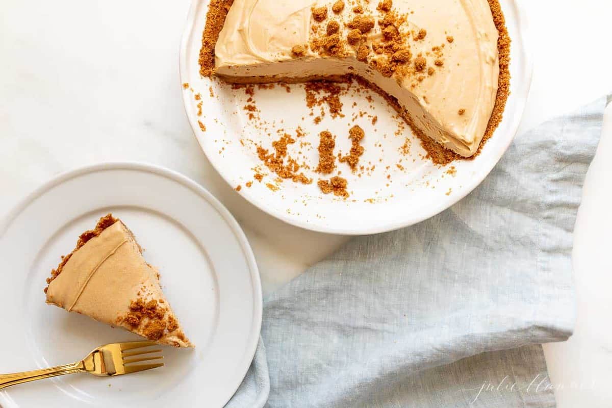 A cookie butter cheesecake with a speculoos crust, several slices gone. White plate with a slice of cheesecake to the side.