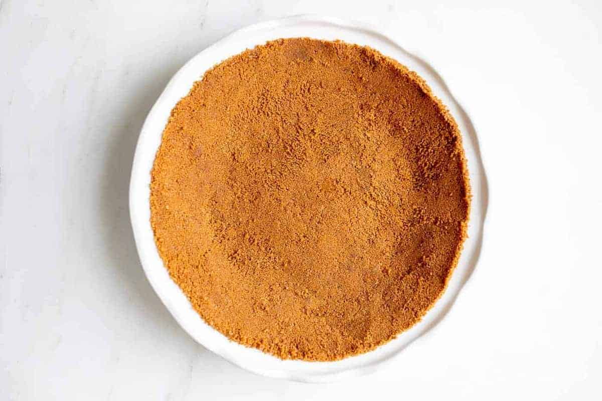 A white pie pan full of speculoos cookie crust for a pie.