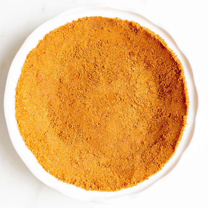 A white pie pan full of speculoos cookie crust for a pie.