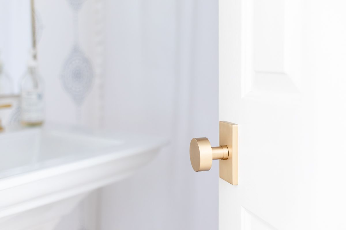 Update a home with new brass door knobs like this image: A bathroom with a white pedestal sink, blue and white striped bathroom, and a brass door knob