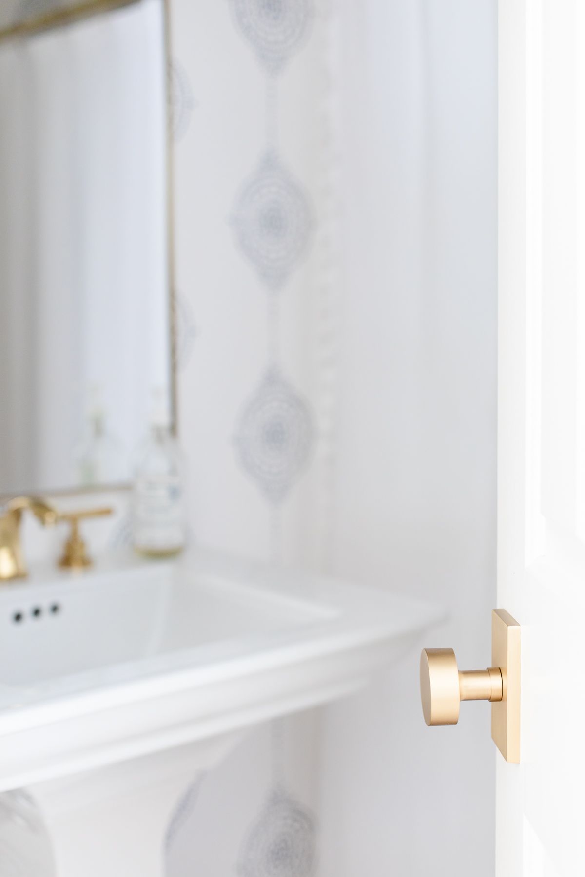 A bathroom with a white pedestal sink, blue and white striped bathroom, and a brass door knob for a house update