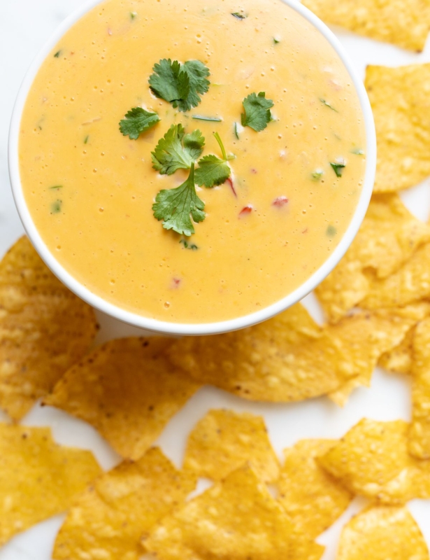 A white bowl full of Velveeta cheese dip surrounded by tortilla chips.