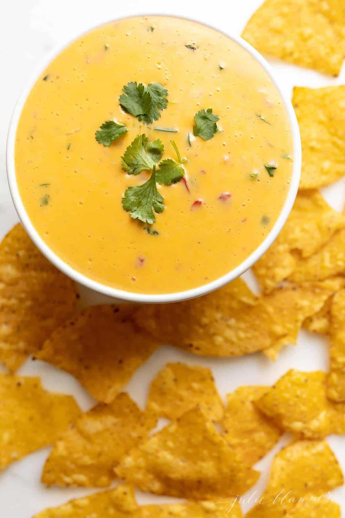 A white bowl full of cheese dip surrounded by tortilla chips.