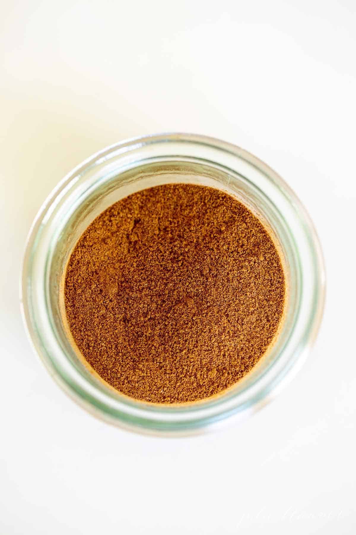 A small clear jar filled with a homemade apple pie spice blend.