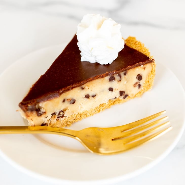 A white plate with a slice of cookie dough pie and a gold fork.