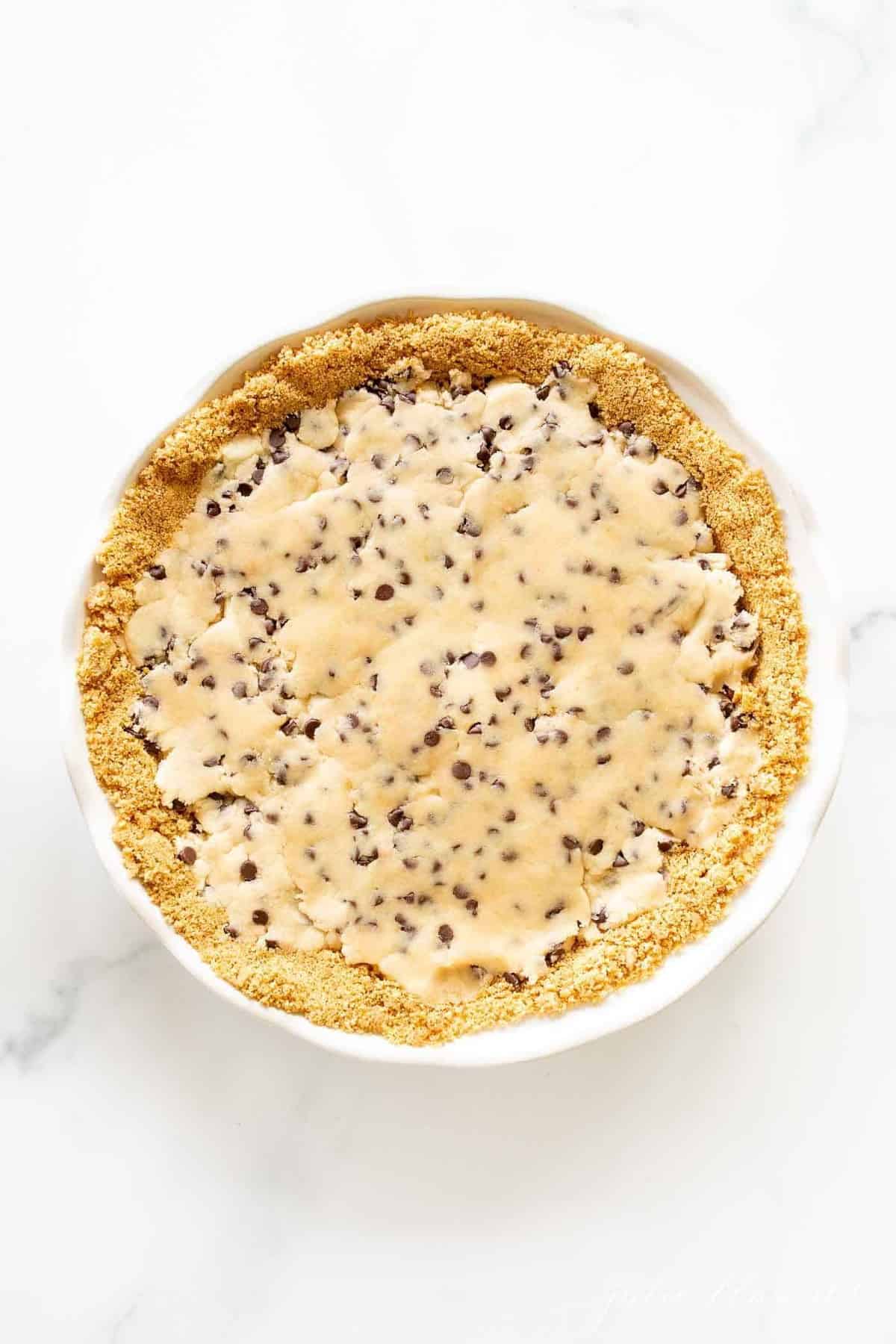 Cookie dough pie filling inside a homemade pie crust on a marble surface.