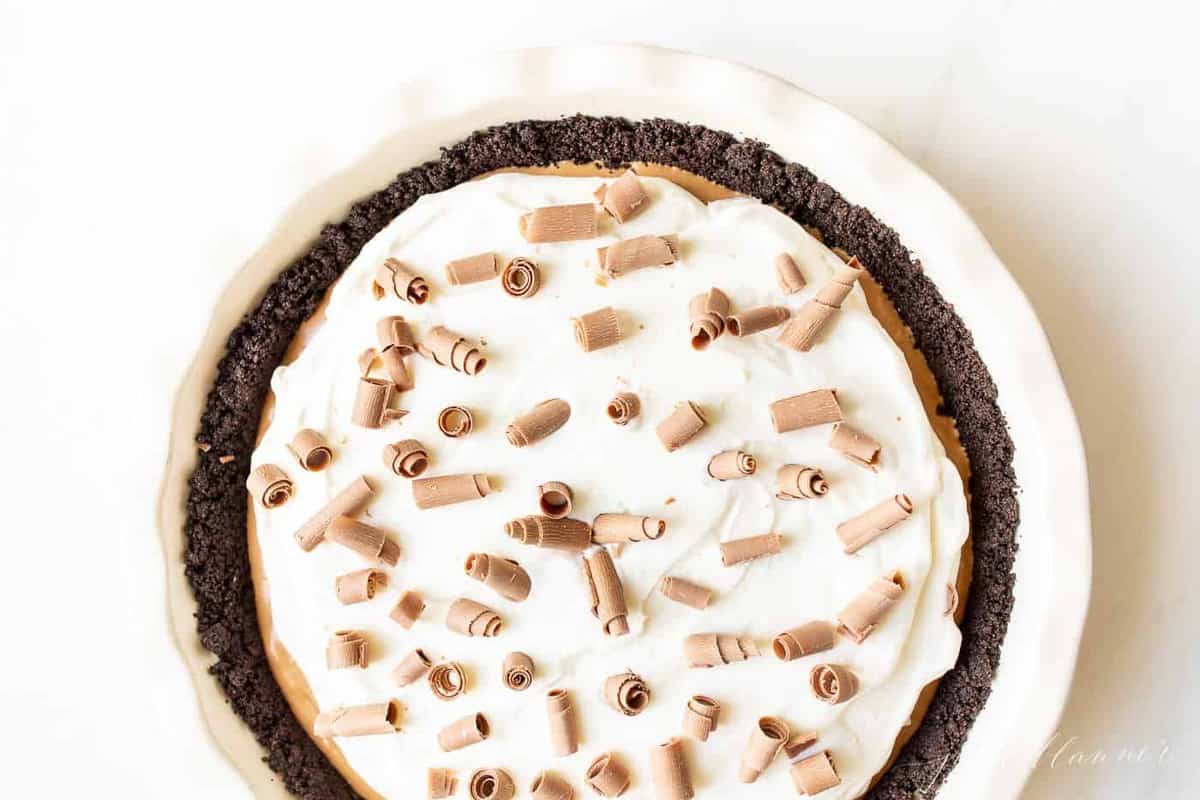 A white pie plate filled with a french silk pie recipe, placed on a marble surface and covered in chocolate shavings.
