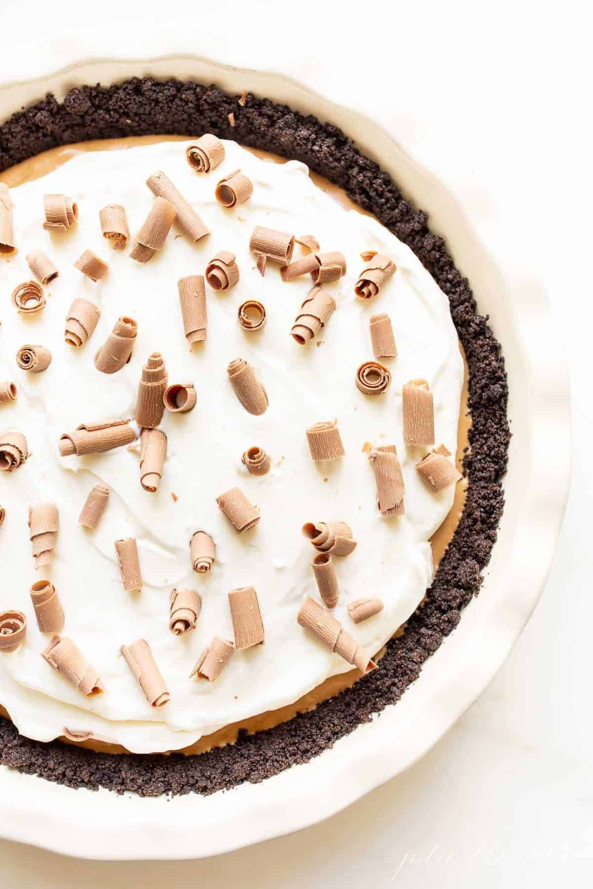 A white pie plate filled with a french silk pie recipe, placed on a marble surface and covered in chocolate shavings.