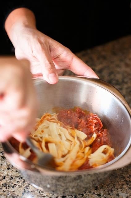 Hands mixing fresh homemade pasta in a stainless steel bowl.