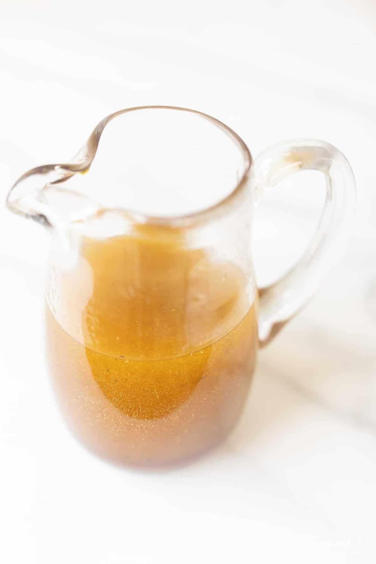 Marble surface with a small pitcher full of an easy homemade vinaigrette recipe.
