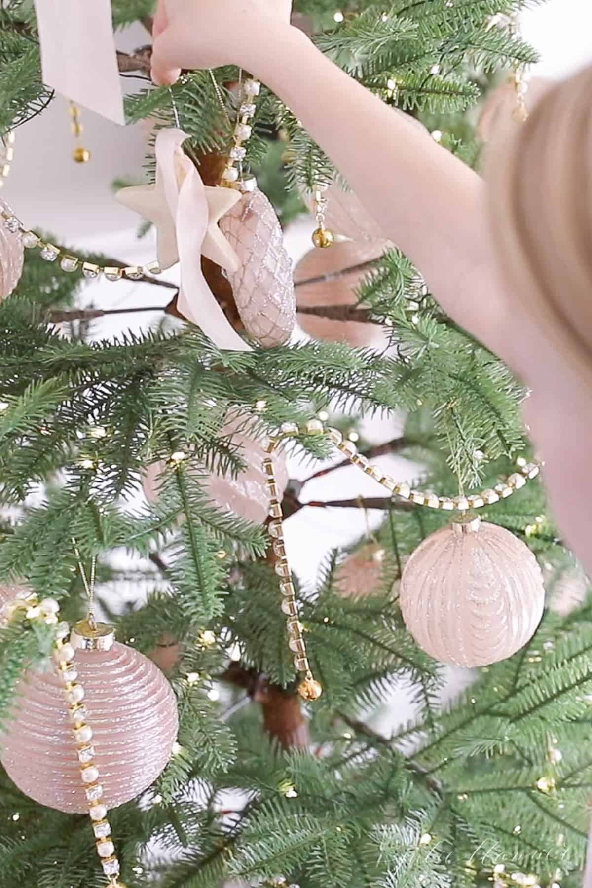 Tepi wajah dan tangan seorang gadis kecil saat dia meletakkan hiasan adonan garam buatan sendiri di pohon Natal.