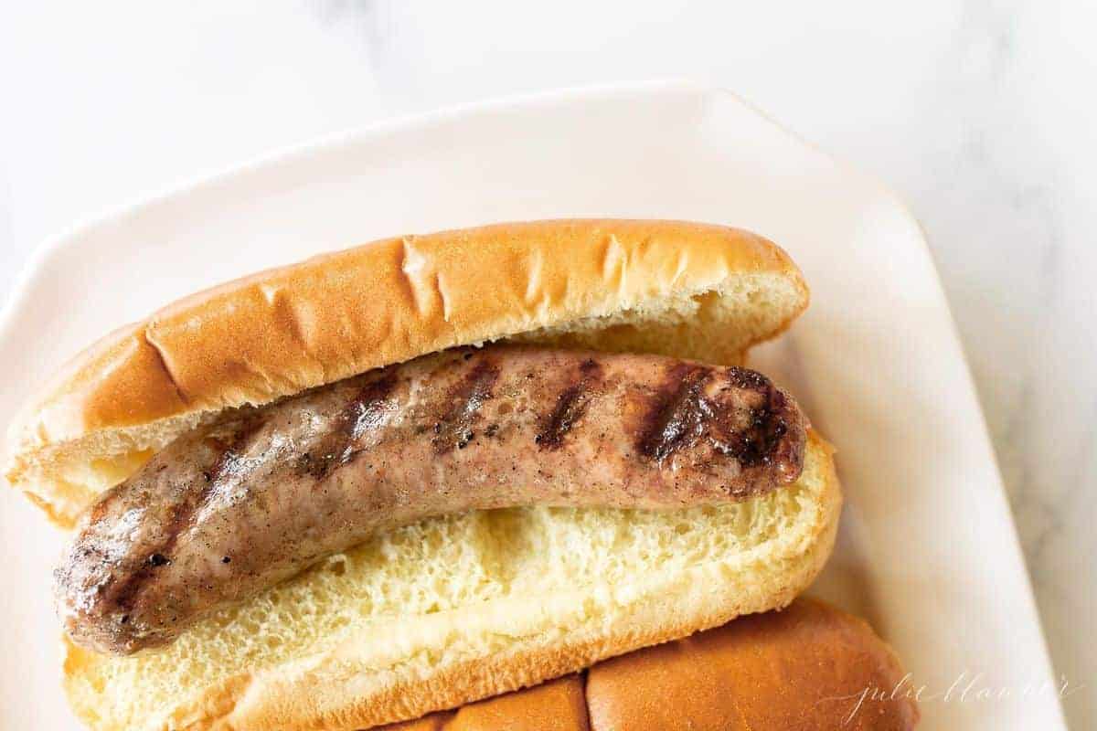 A grilled bratwurst in a bun on a white plate.