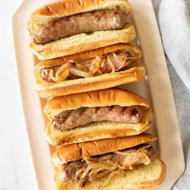 A white tray filled with bratwurst sausages in buns.