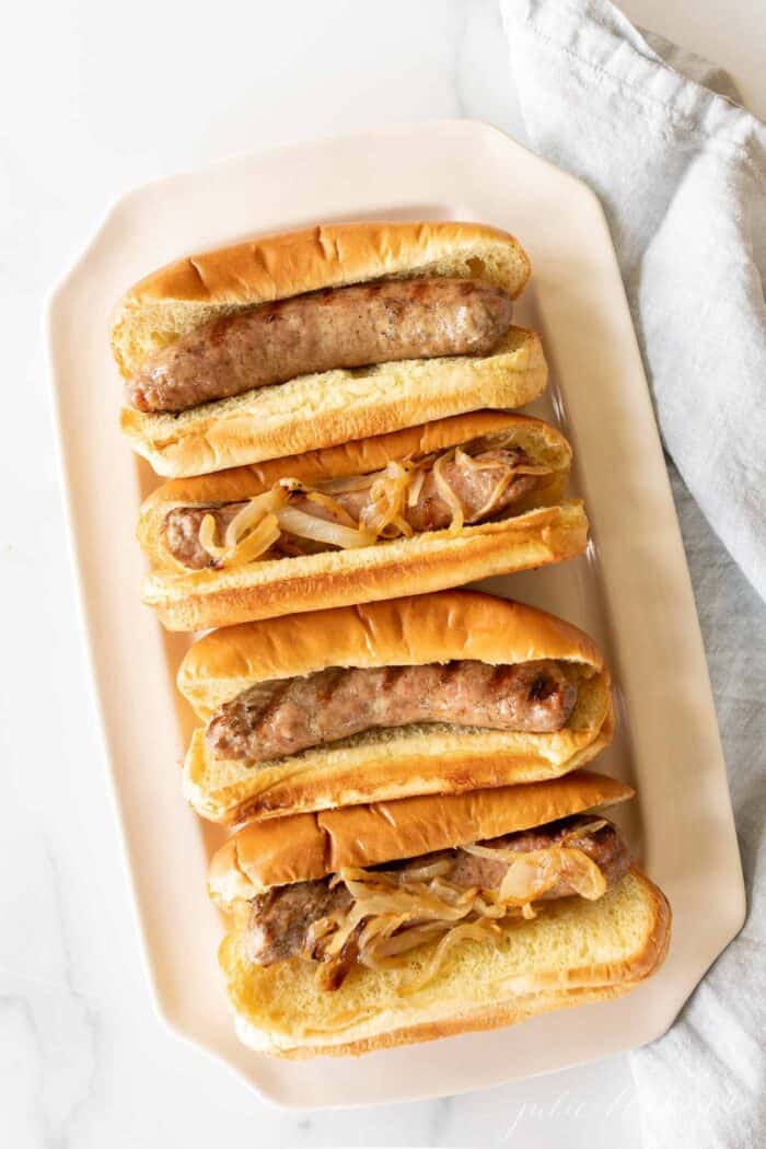 A white tray filled with bratwurst sausages in buns.