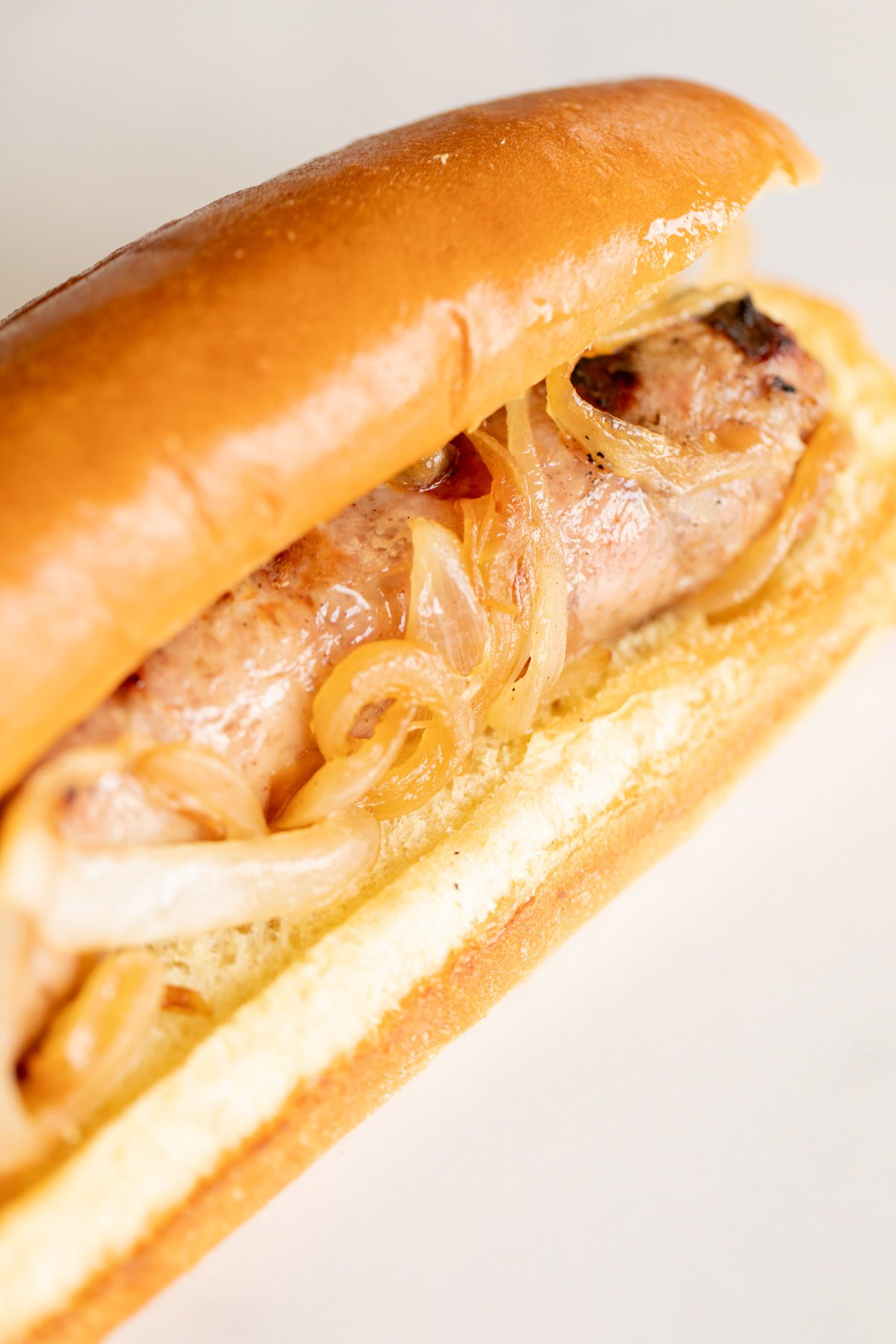 A sausage in a hot dog bun topped with caramelized onions on a white background showcases the art of cooking bratwurst.