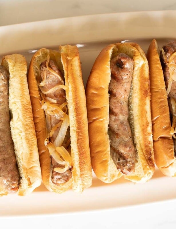 A white tray filled with bratwurst sausages in buns.